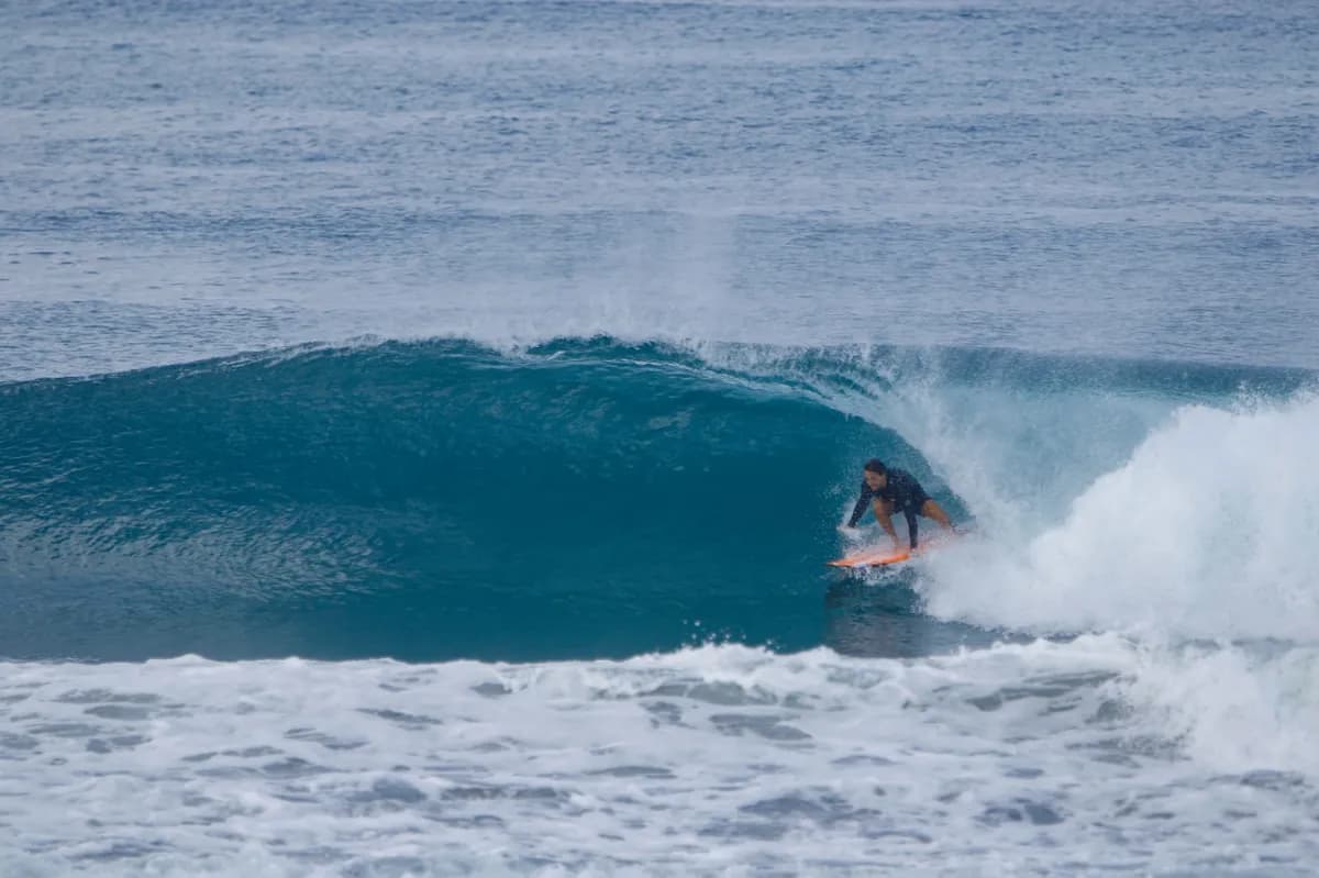 Surfer crouching inside a crystal clear blue barrel wave.