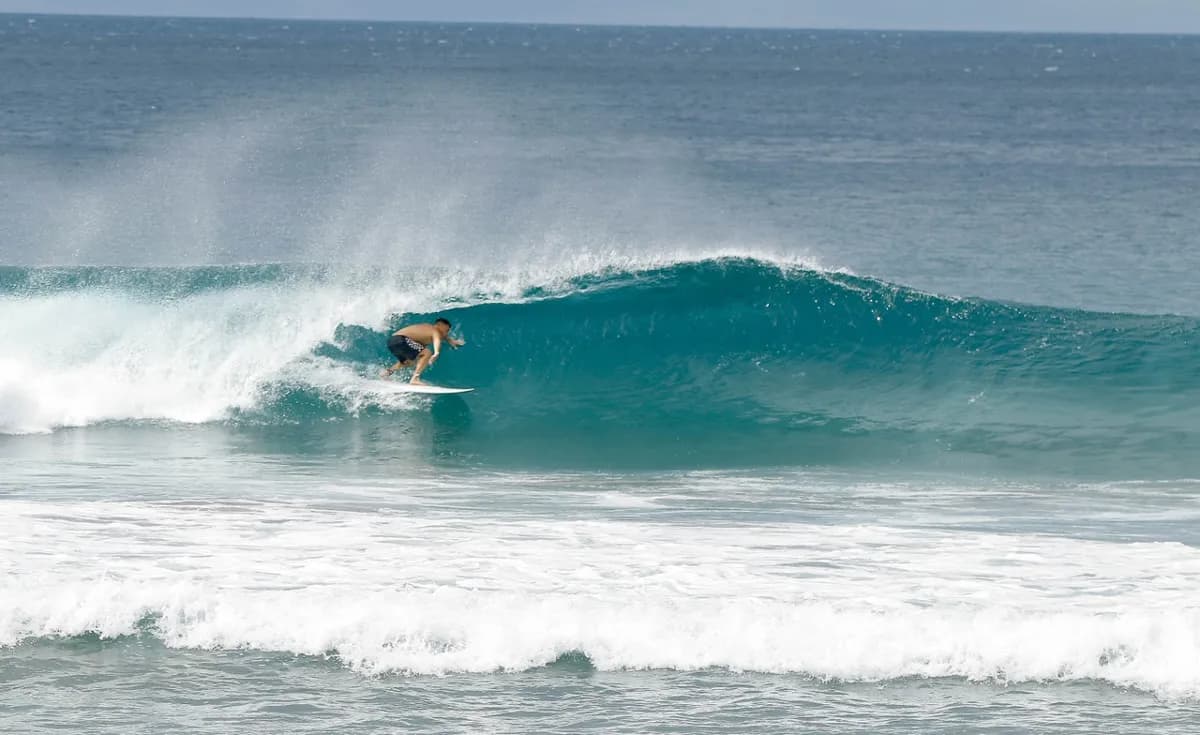 Surfer skillfully rides inside a clear blue barrel wave.