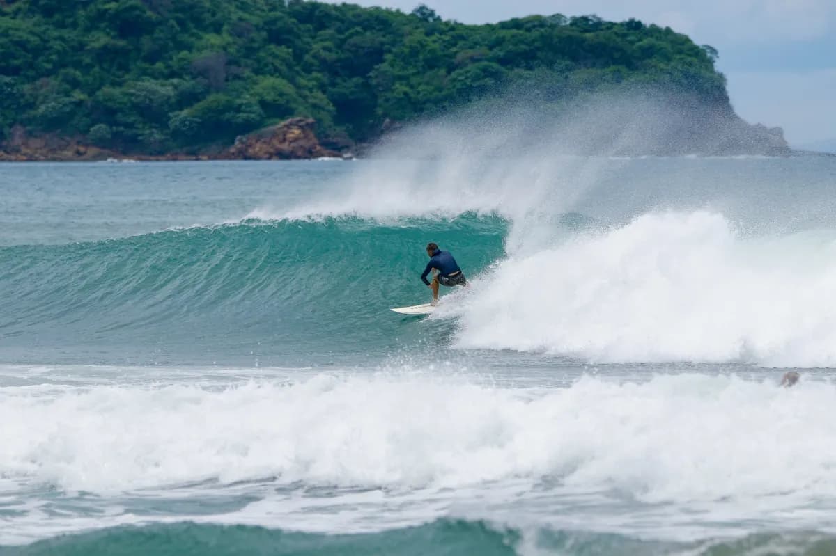 Surfer crouches inside a clear, green barrel wave.