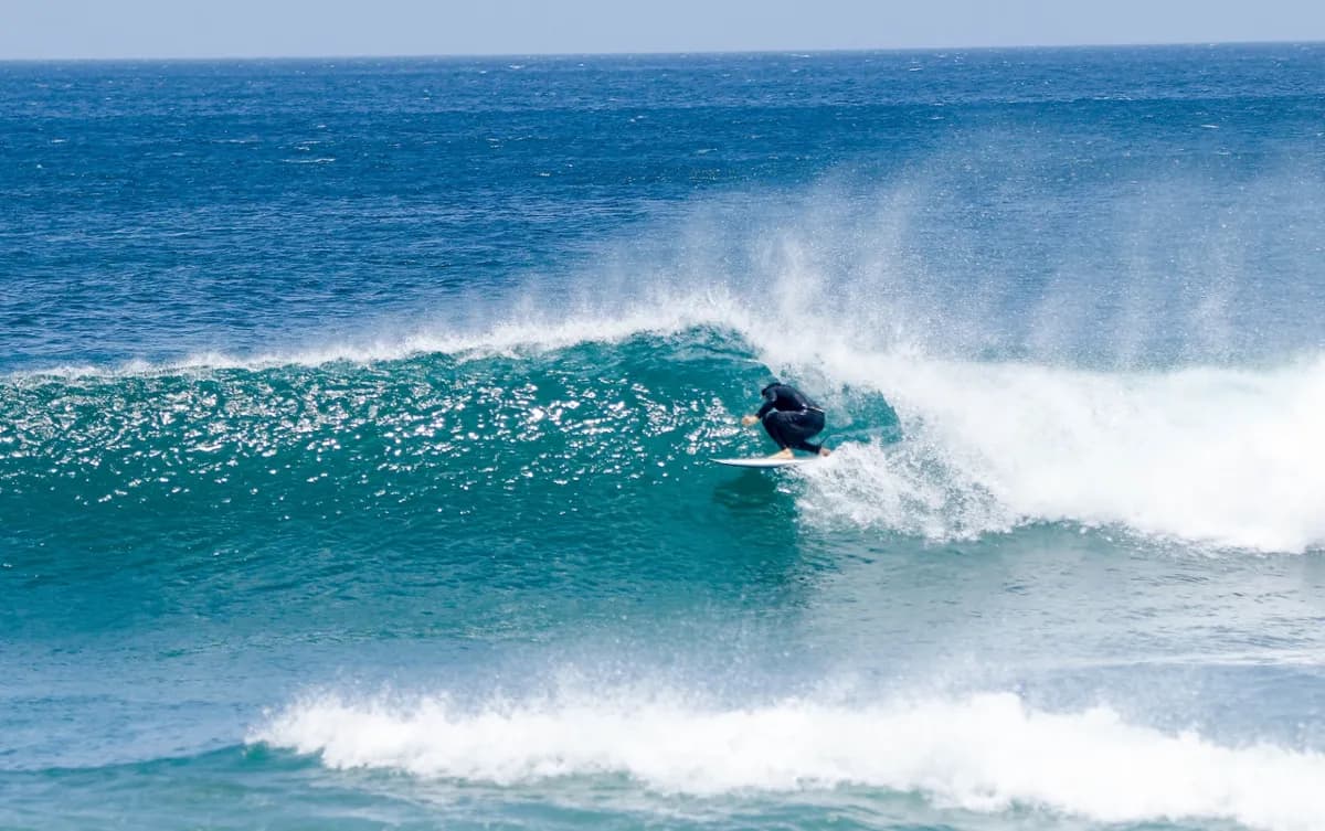 Surfer rides inside a clear blue wave barrel.