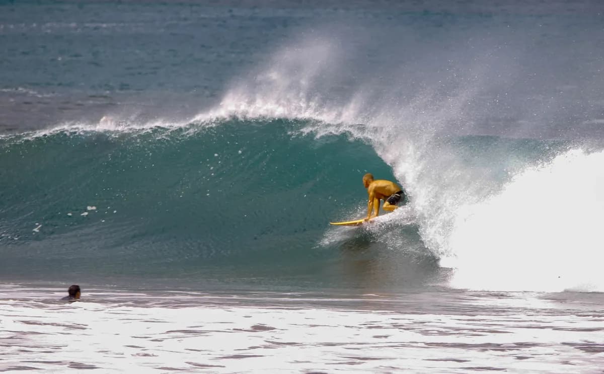 Surfer in yellow rides a powerful wave barrel.