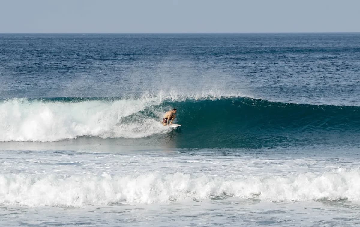 Surfer crouching inside a blue-green barrel wave.