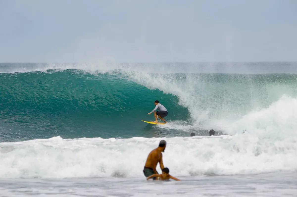 Surfer rides a perfect barrel wave with others watching.