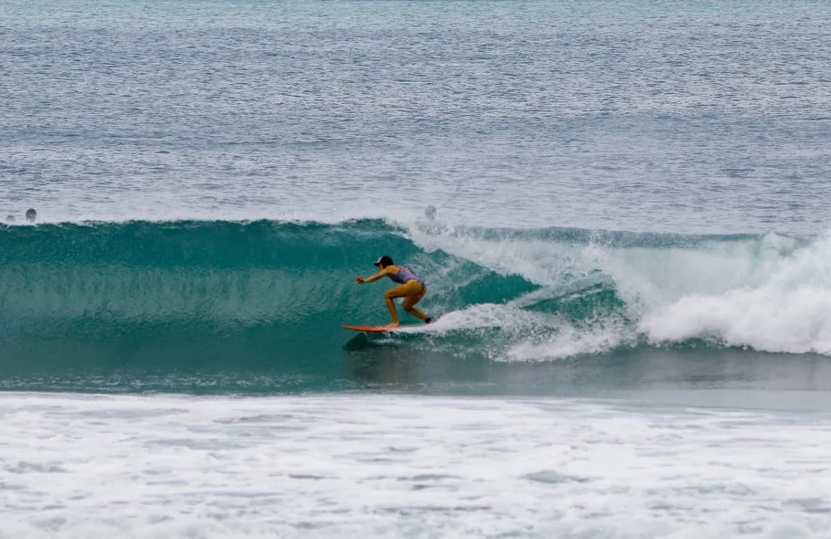 Surfer riding a turquoise wave under a grey sky.