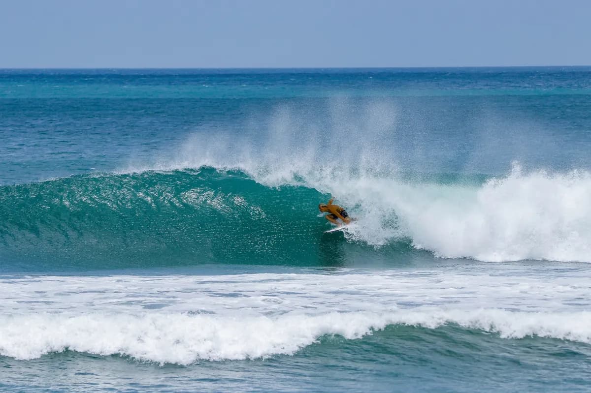 Surfer tucked into a perfect barrel on a turquoise wave.