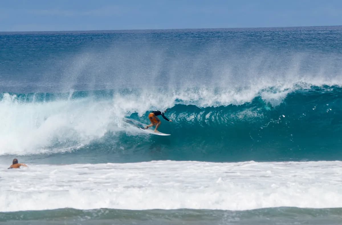 Surfer skillfully rides inside a hollow wave, maintaining balance.