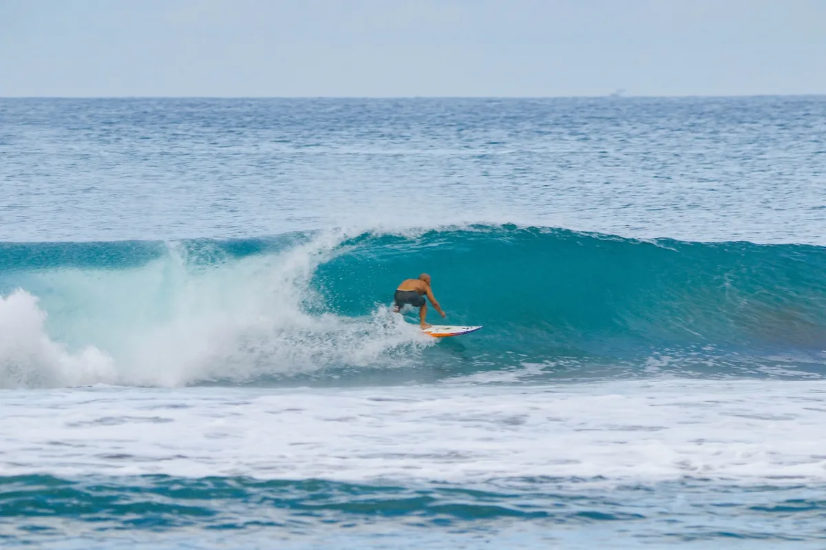 Surfer crouches inside a perfect blue barrel wave.