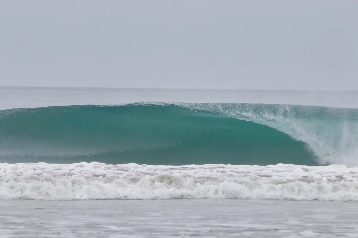 Perfect empty wave barrels under a cloudy sky.