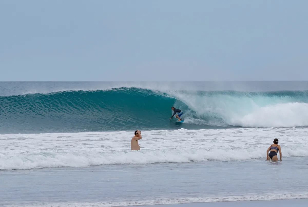 Surfer crouches inside a clean barrel with observers nearby.