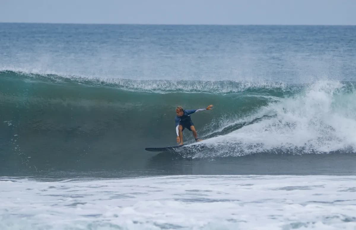 Surfer performs a stylish bottom turn under a curling wave.