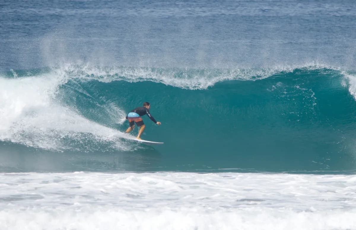 Surfer rides smoothly inside a clear blue barrel.
