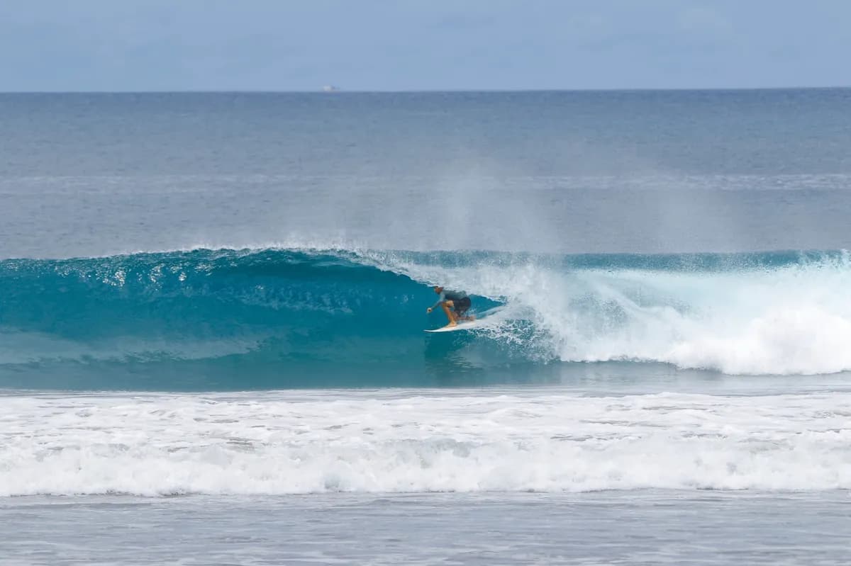 Surfer rides inside a crystal-clear blue barrel.