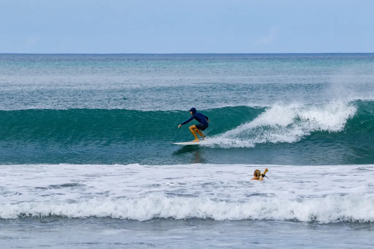 Surfer rides a clean right-hand wave while paddler watches.