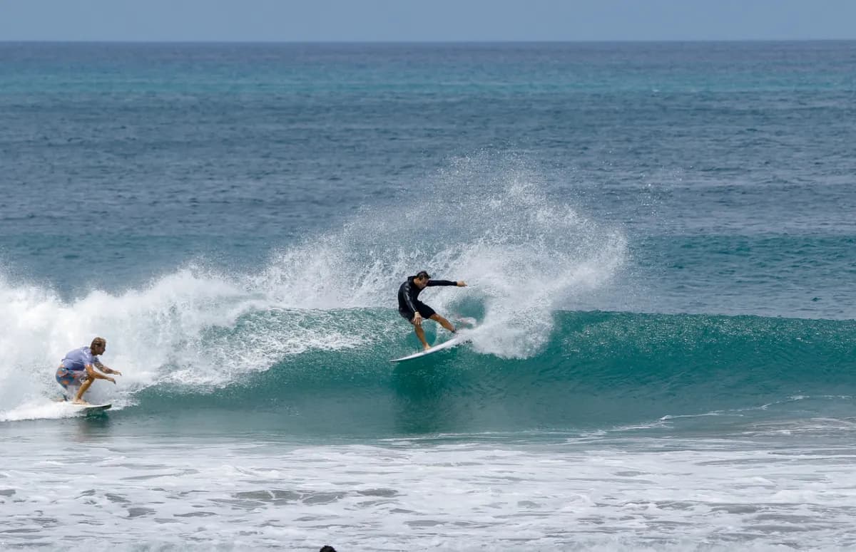 Surfers execute synchronized cutbacks on a small wave.