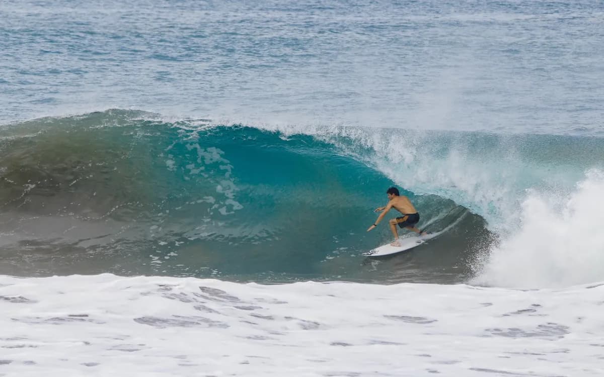 Surfer tucked in a crystal clear barrel, skillfully riding.