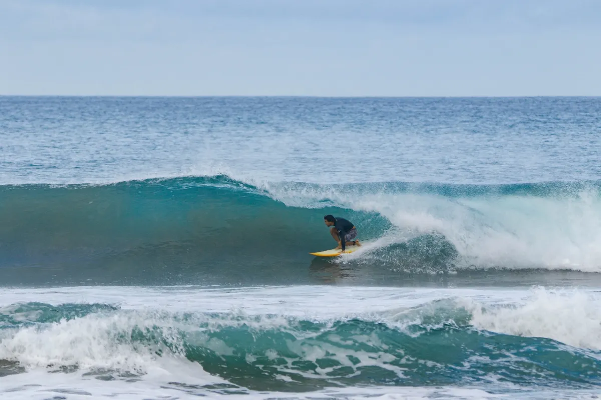 Surfer crouching inside a translucent blue barrel wave.