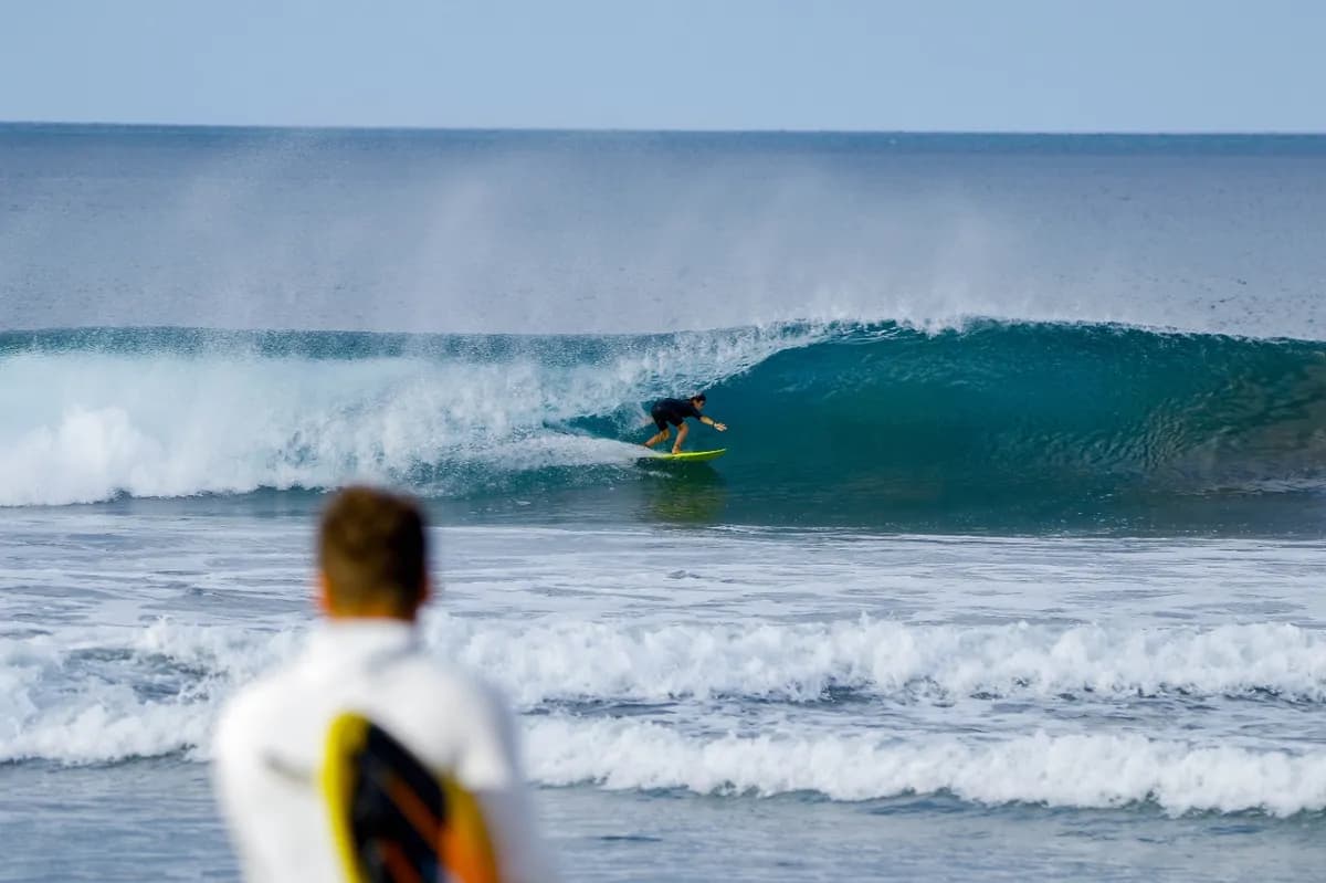Surfer crouches inside a perfect barrel as observer watches.