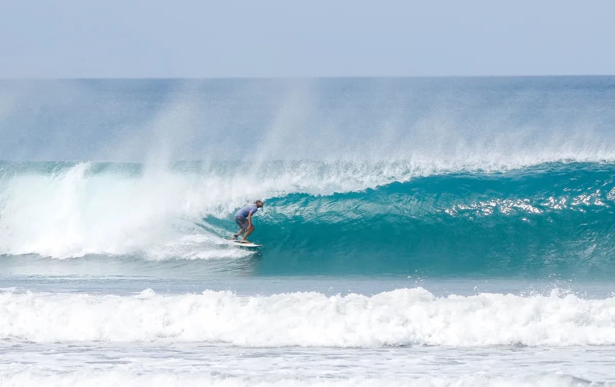 Surfer carves inside a sparkling blue barrel wave.