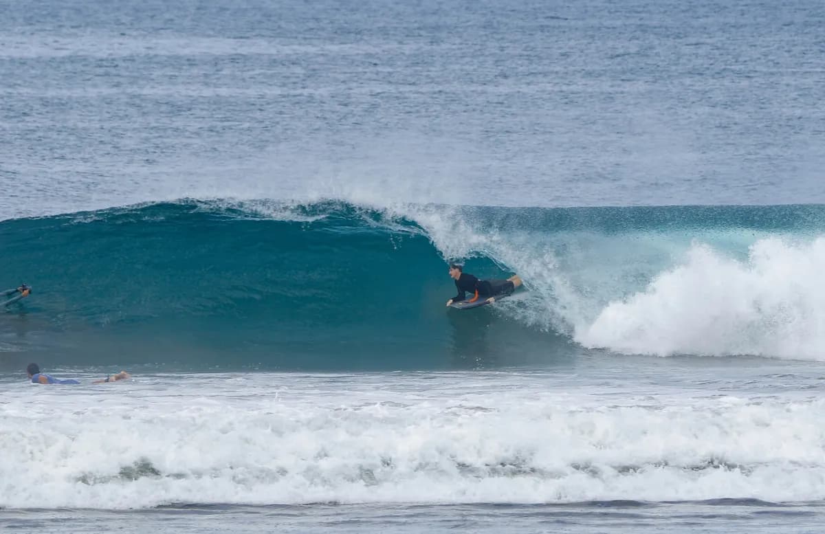 Surfer crouches inside a perfect blue barrel.