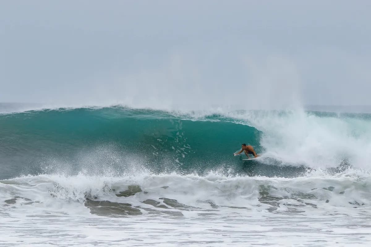 Surfer tucked under green barrel wave with misty spray.