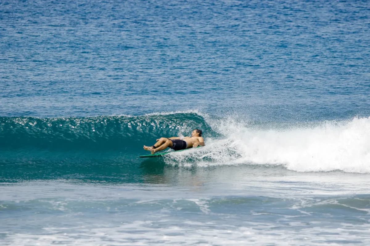 Surfer bauti-yelos is lying flat on a small wave.