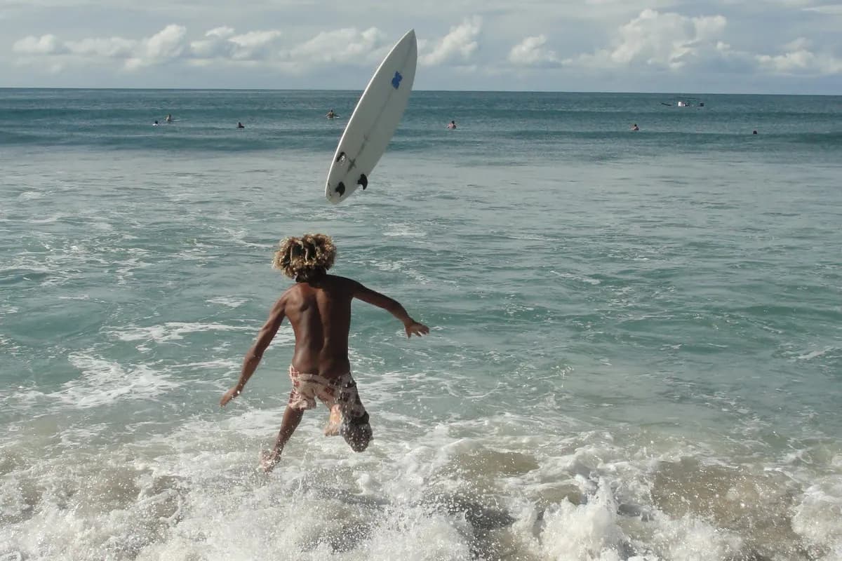 Surfer leaps as board flies above.