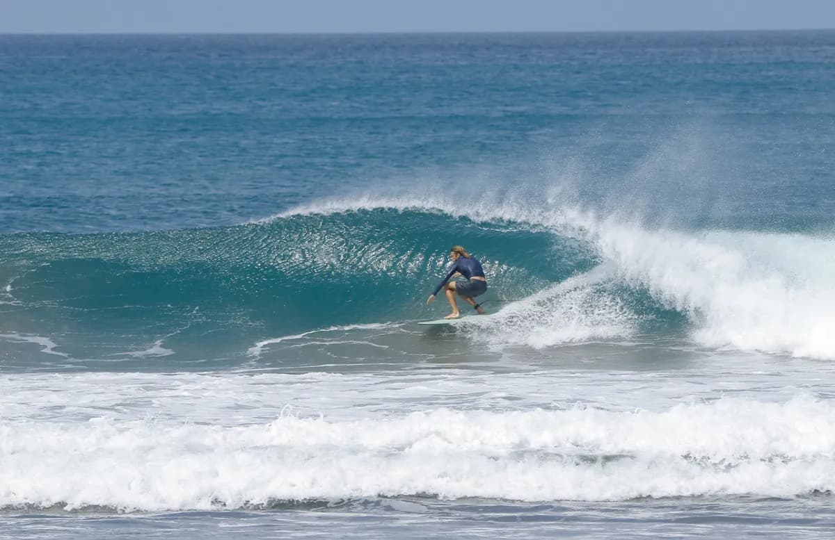 Surfer crouches low inside a crystal blue barrel.