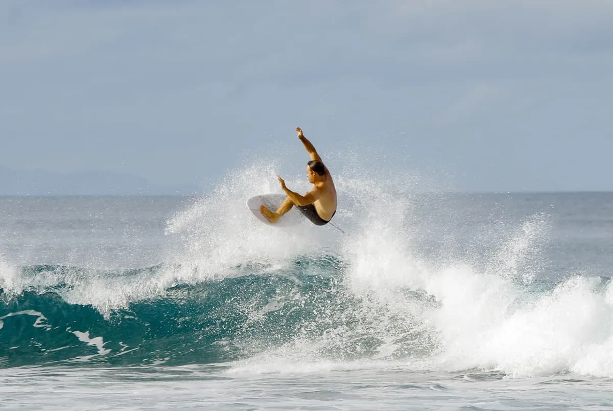 Surfer performs a stylish air above crashing waves.