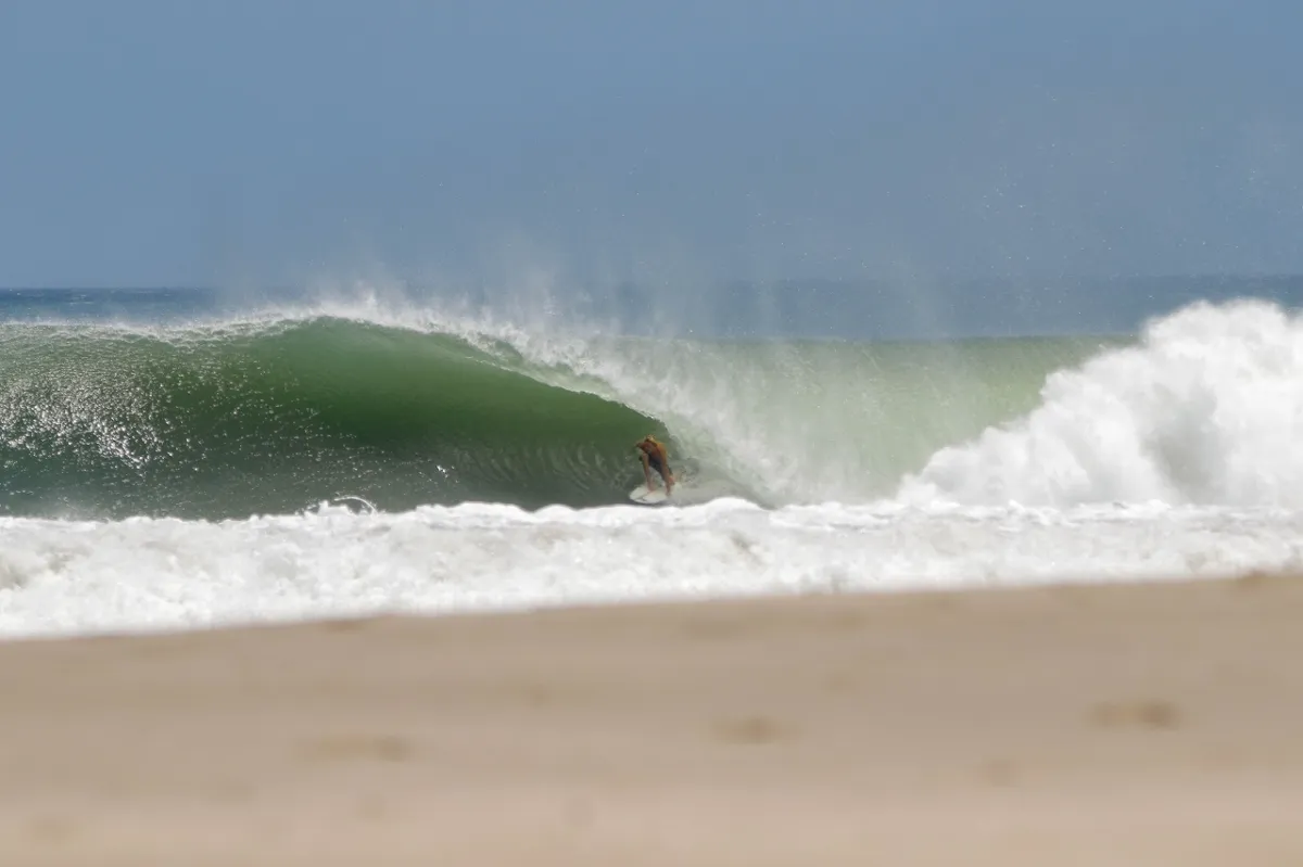 Surfer tucks into a powerful green barrel near the beach.