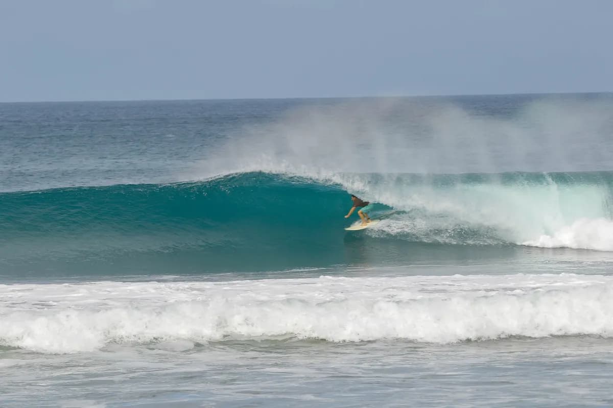 Surfer rides a perfect barrel in clear blue water.