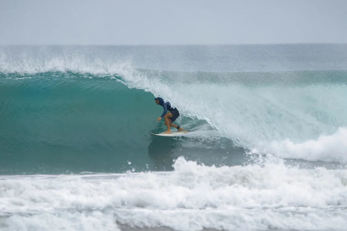 Surfer crouches inside a perfect turquoise barrel.