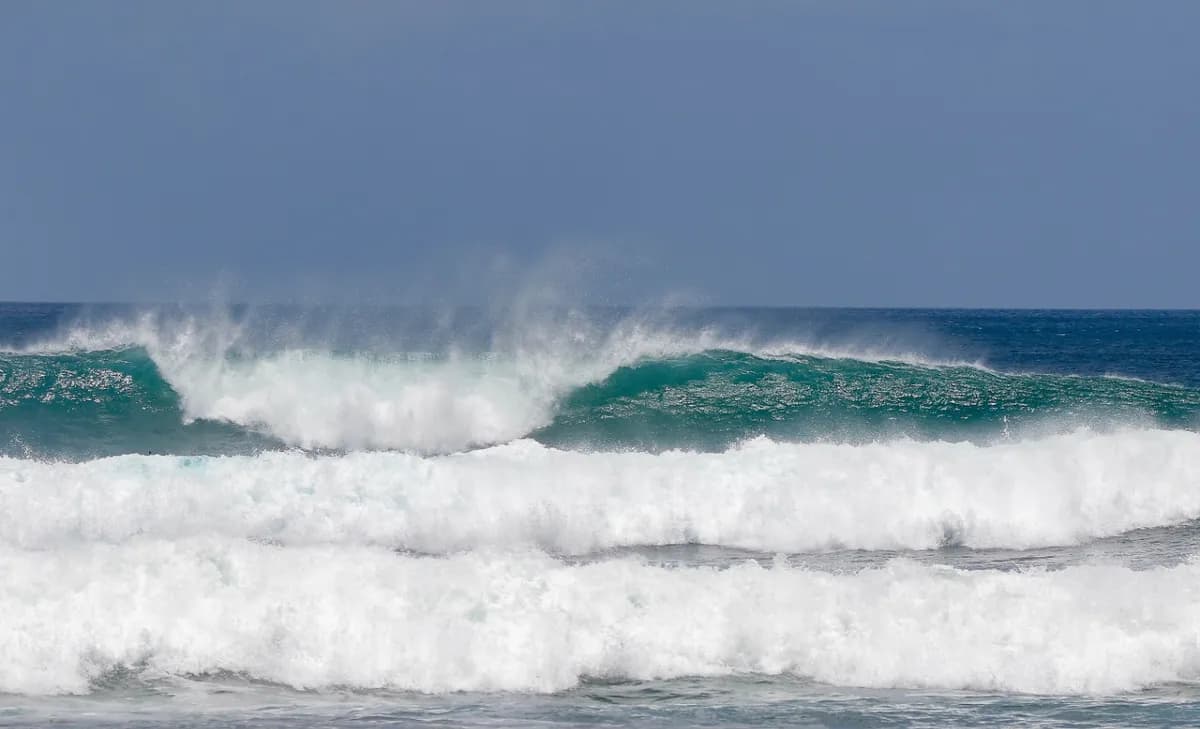 Strong wave breaks with misty spray beneath blue sky.