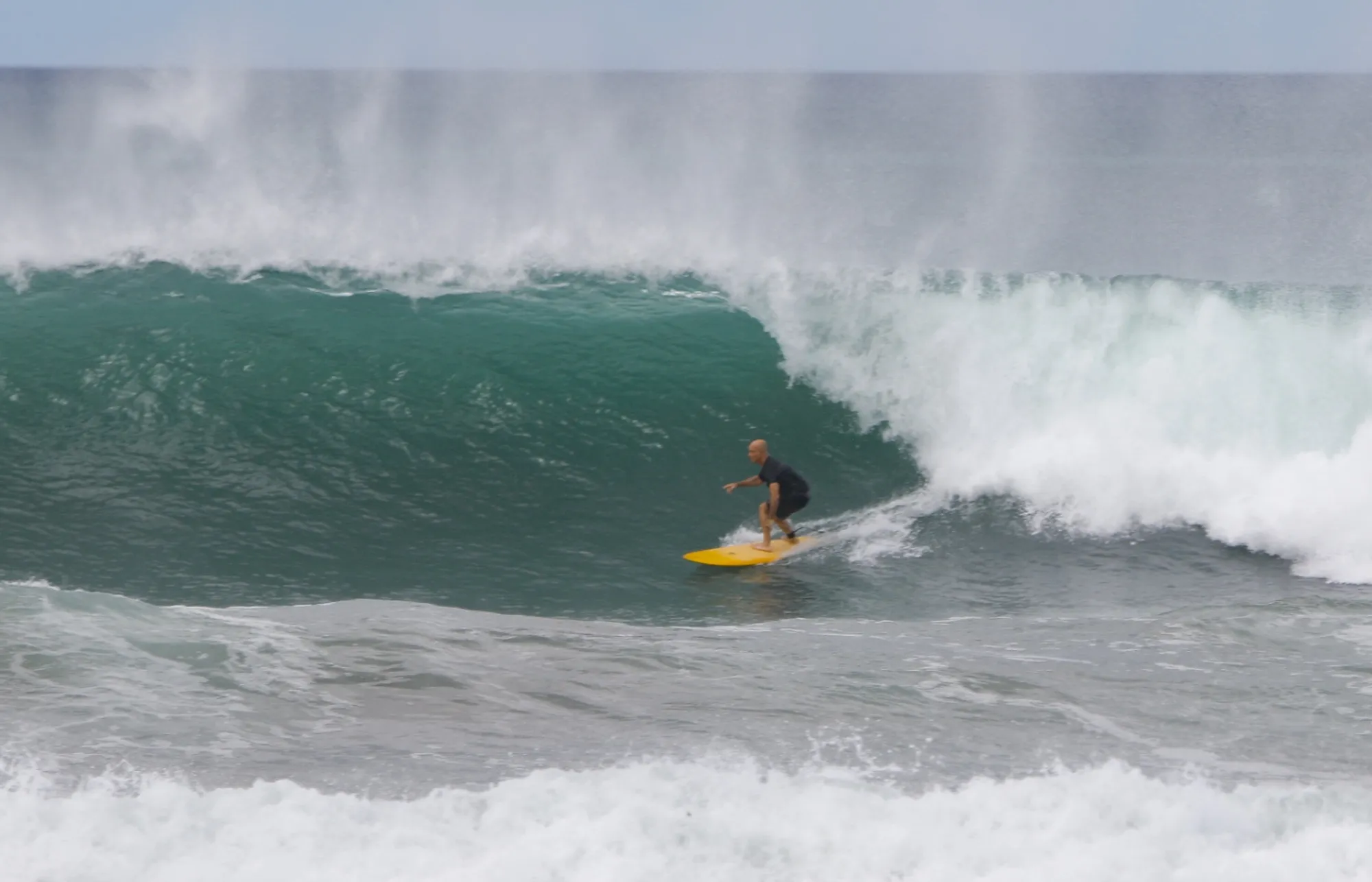 Surfer rides a powerful green barrel on a yellow board.