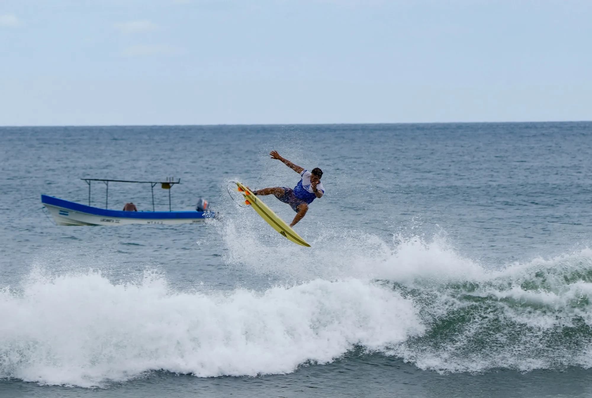 Surfer executes a high air as a boat passes in the background.